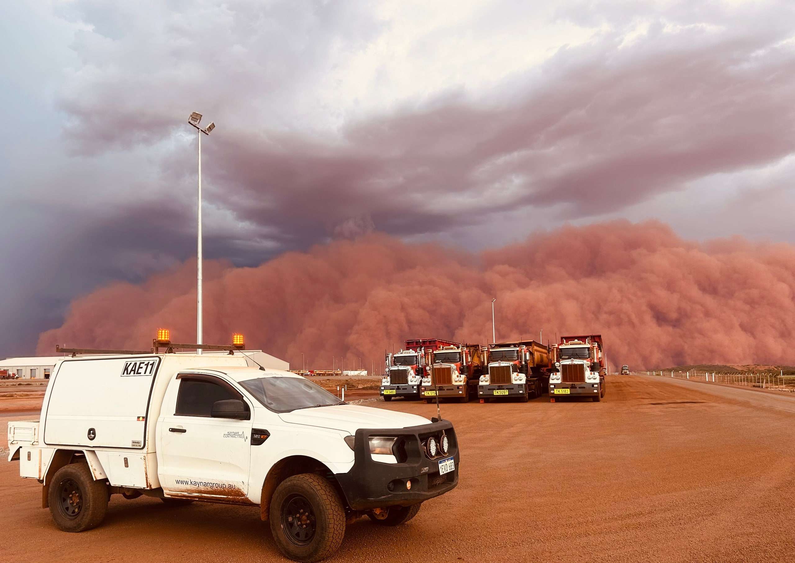 Kaynar service ute KAE11 in the foreground with four road trains lined up behind it as a towering red dust storm rolls in