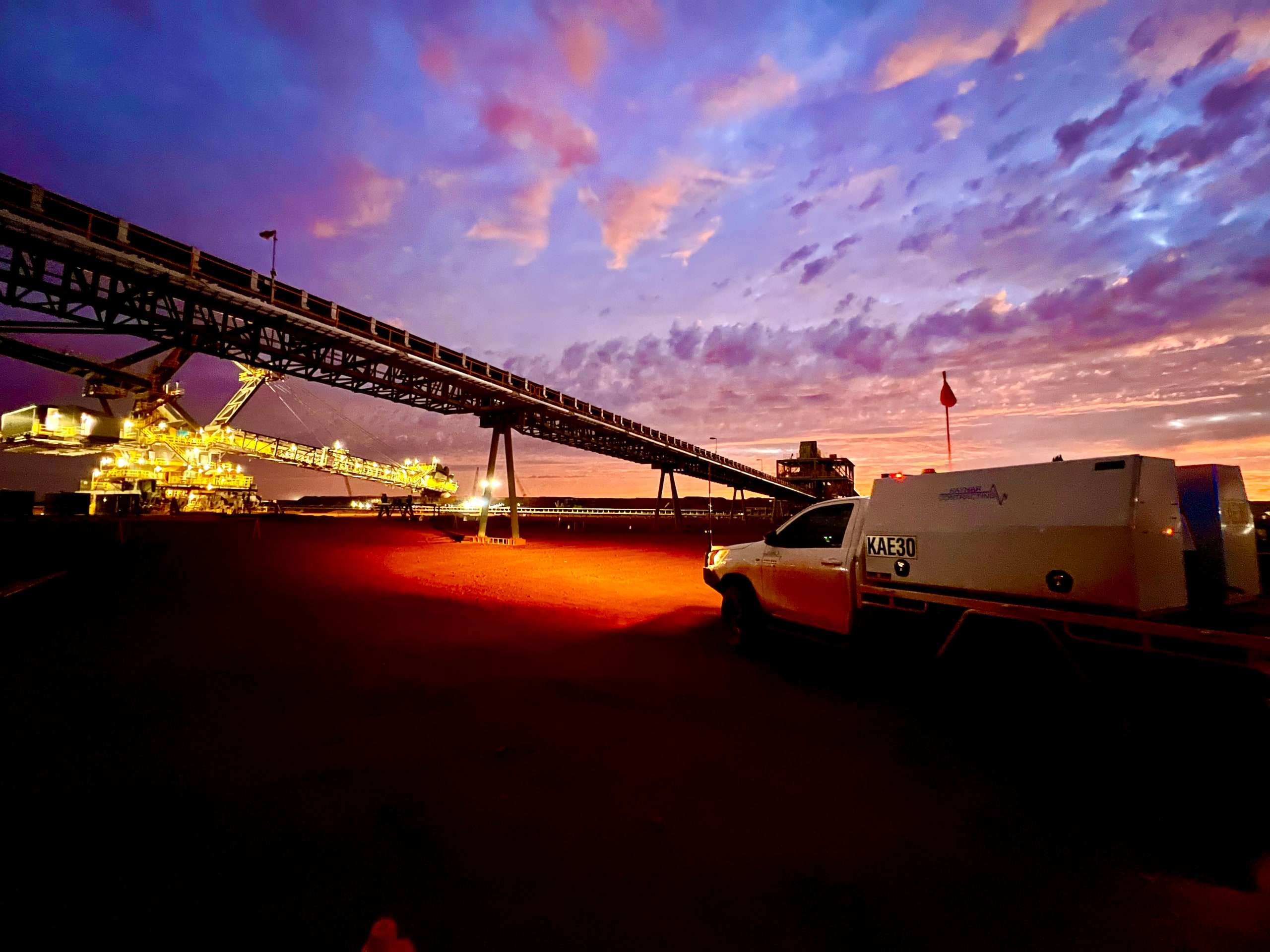 Kaynar service ute KAE30 parked beside a mine site conveyor and lit stacker under a purple and orange sunset sky