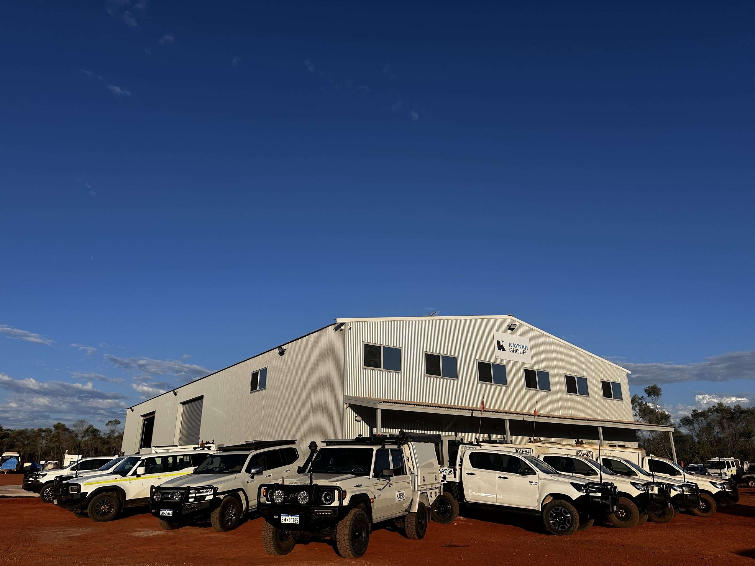 The Kimberley Maintenance Centre workshop building with Kaynar Group signage and a row of white Kaynar utes parked out front on red dirt under a clear blue sky